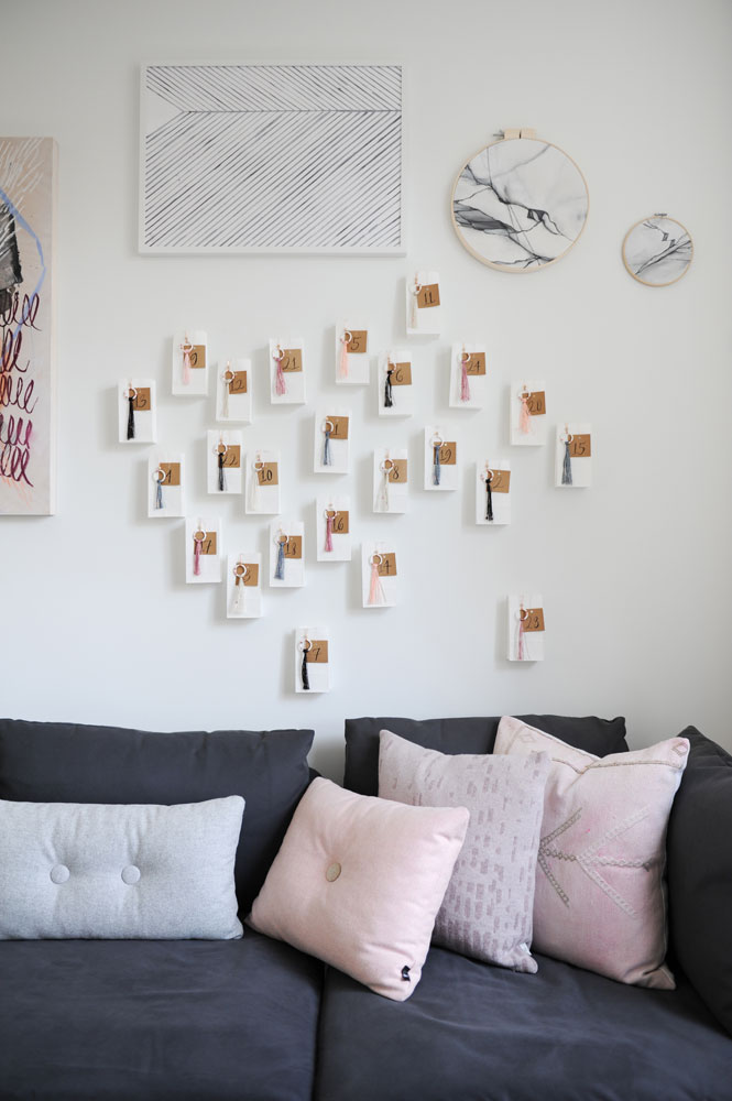 number and tassel cards on wall above dark grey sofa with pink cushions