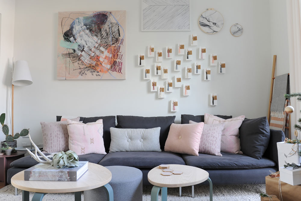 living room, dark grey sofa with pink cushions, tassel and number tags on wall with four other art pieces