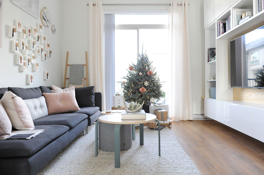 living room with small xmas tree in window, grey sofa facing wall unit with TV in it