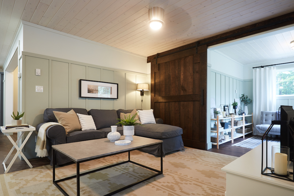 rustic green-and-grey cottage living room with brown barn door open to grey flex room