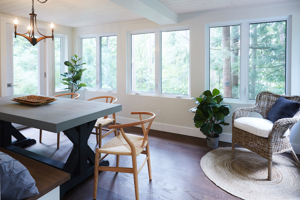 white sunroom with grey dining table and windows showing view of green forest