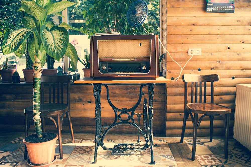 An antique radio sits on a small antique in a rustic wood home surrounded by plants