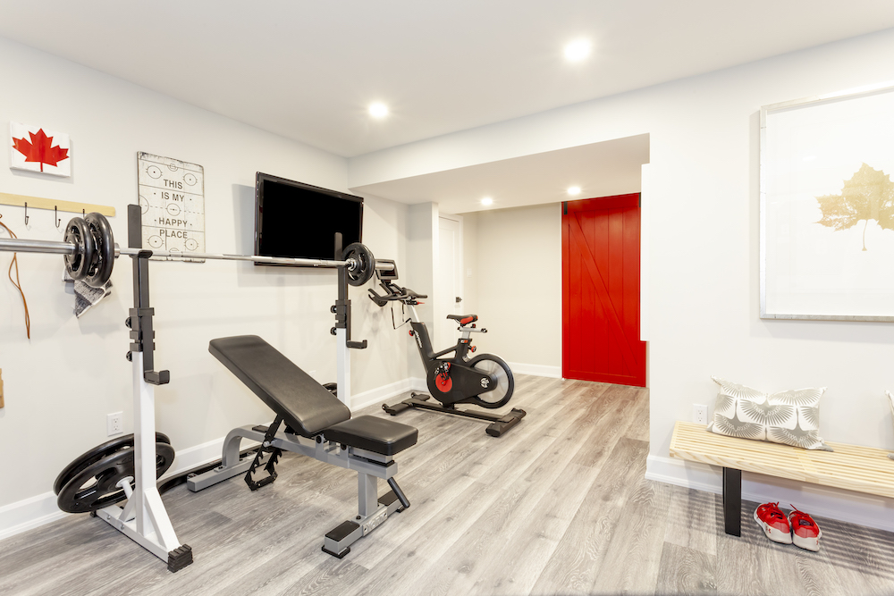 A sleek basement gym with vinyl flooring and exercise equipment against a white wall with a red farmhouse door