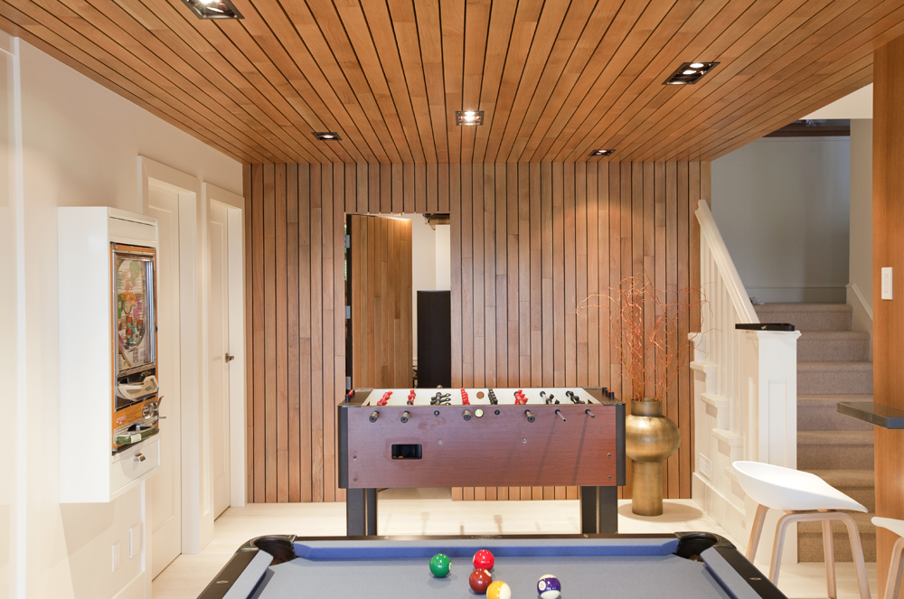 A renovated basement with wood panelled walls with a secret door that opens into a separate room from the games space