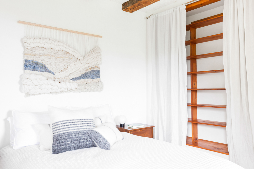 A chic white bedroom with a secret wooden bookshelf tucked away behind flowing white curtains