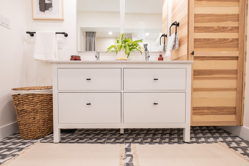 white bathroom with white vanity and tall wood cabinet and patterned tile floor