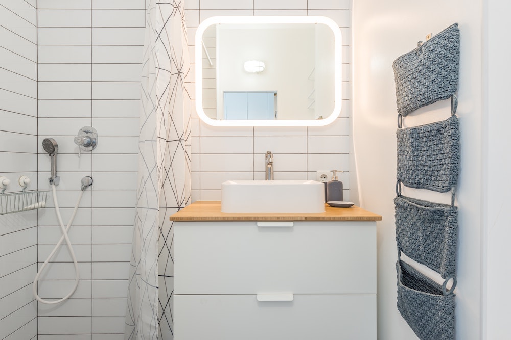modern white bathroom with lighted mirror and tiered hanging storage piece