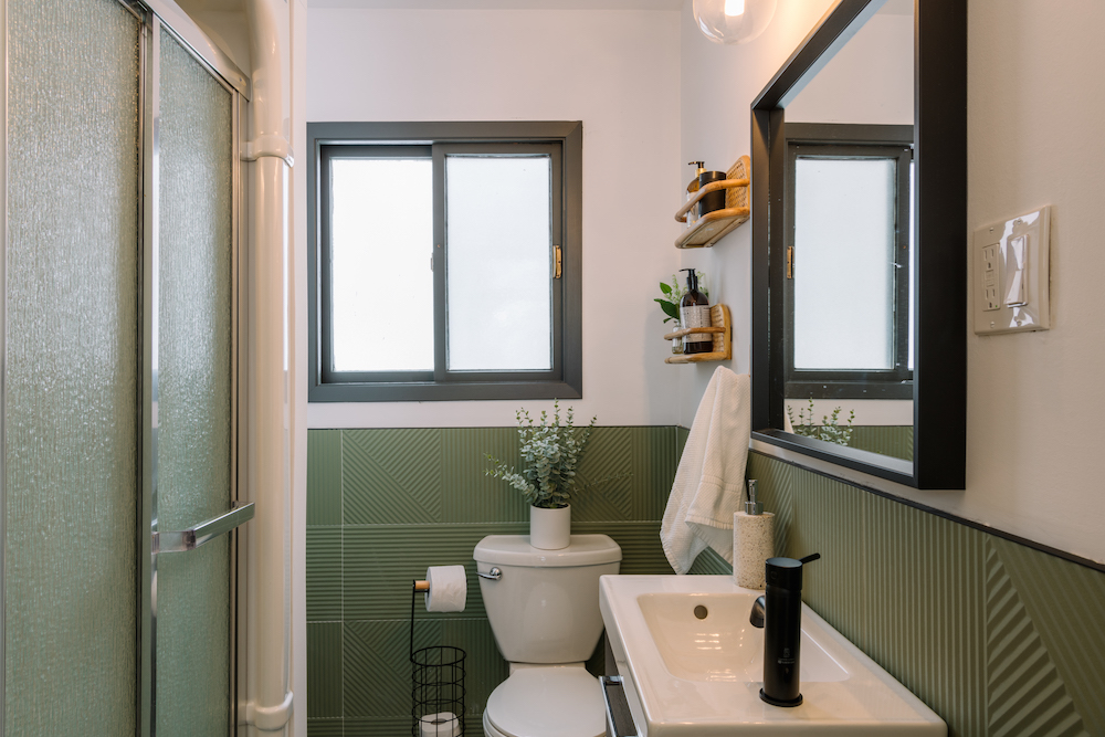 small bathroom with green tiles on wall and brown woven wall shelves