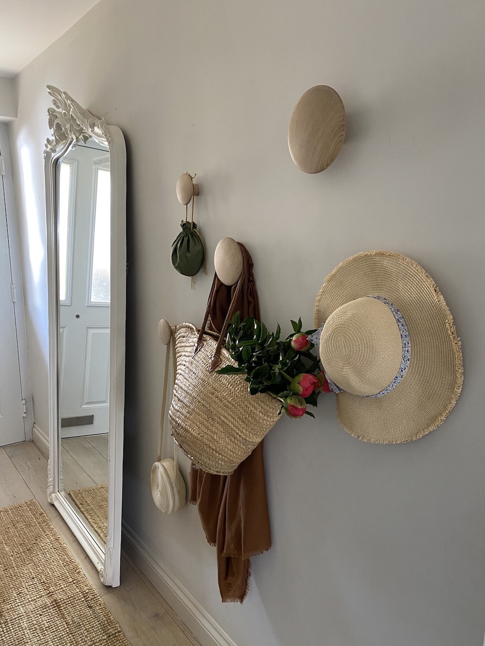Pegs and a standing mirror in a hallway with a sisal runner