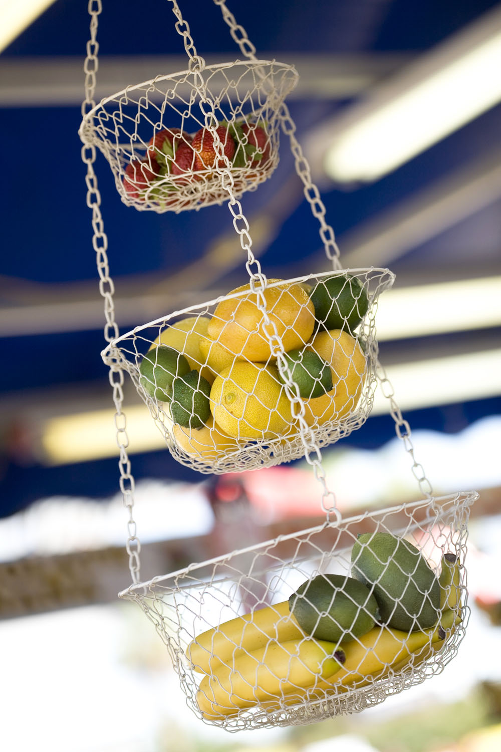 A three-tiered mesh hanging fruit basket filled with bananas, limes, lemons and strawberries