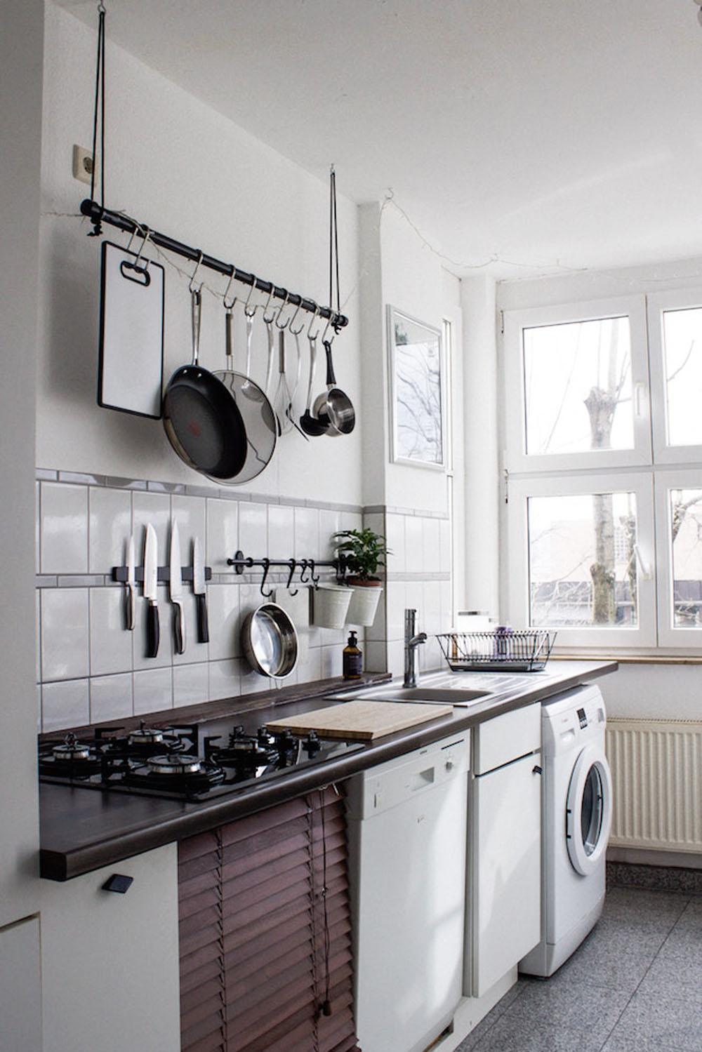 A sleek white kitchen with a magnet strip for knives above the stove and hanging rack for various pots and pans