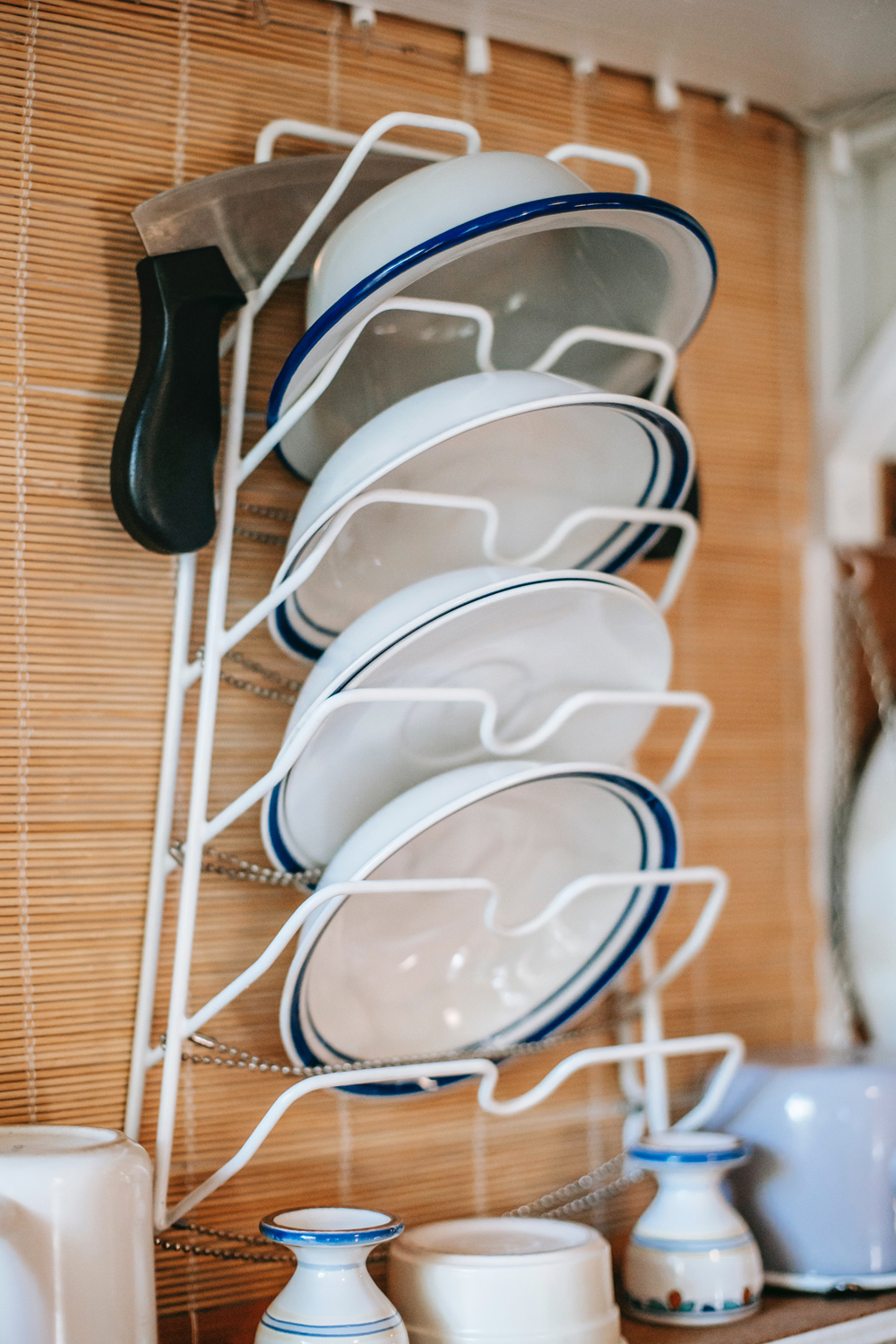 White and blue dinner plates and bowls stacked to dry in a vertical dish rack against a bamboo curtain