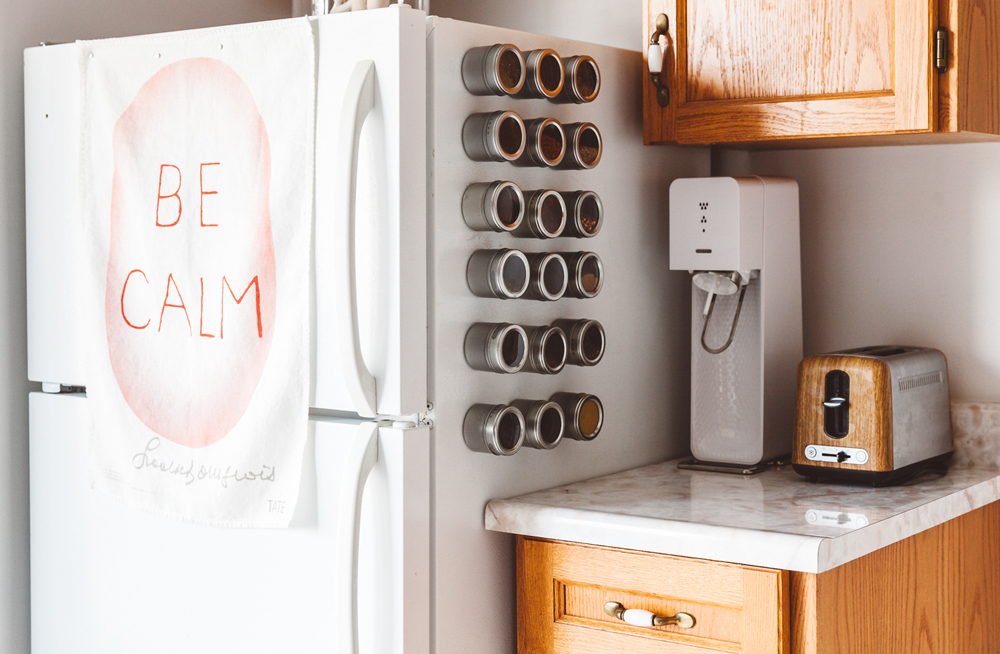 A small kitchen with various magnet spice storage containers on the side of the fridge