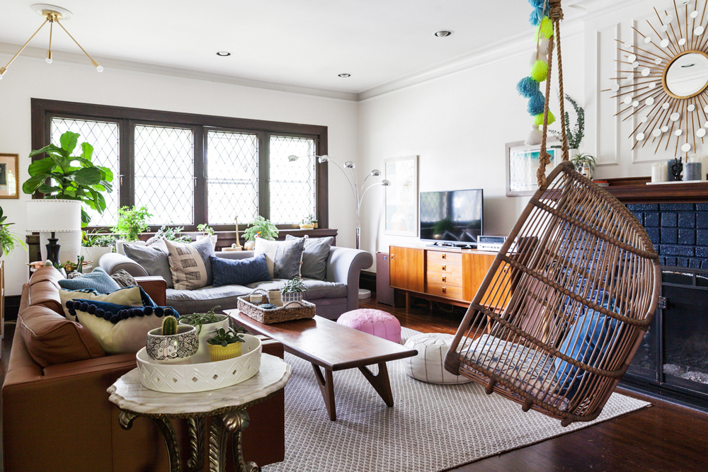 A brightly lit living room with two couches, plenty of throw pillows and a wicker swing