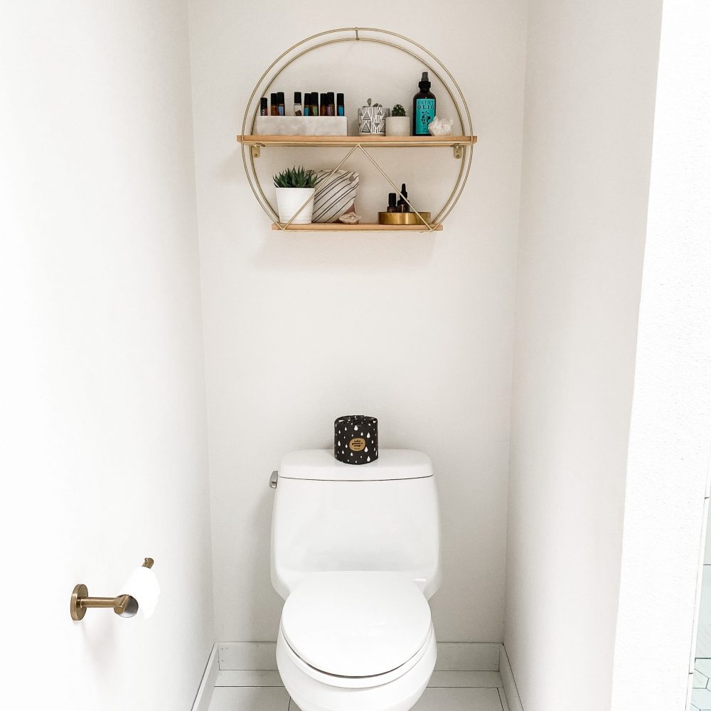 small white bathroom toilet area with shelf filled with toiletries
