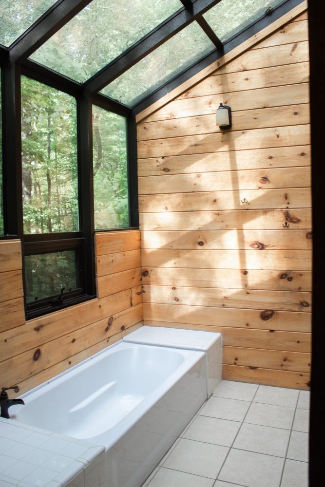 wood-walled bathroom with wall of windows and white bathtub