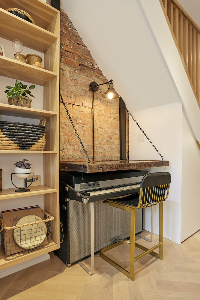 A small space with exposed brick beneath a staircase is transformed into a small music nook complete with keyboards
