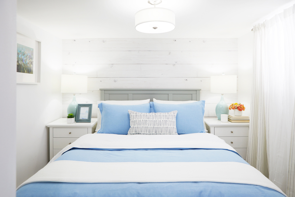 A small white guest bedroom with blue bedsheets and night tables on each side of the bed