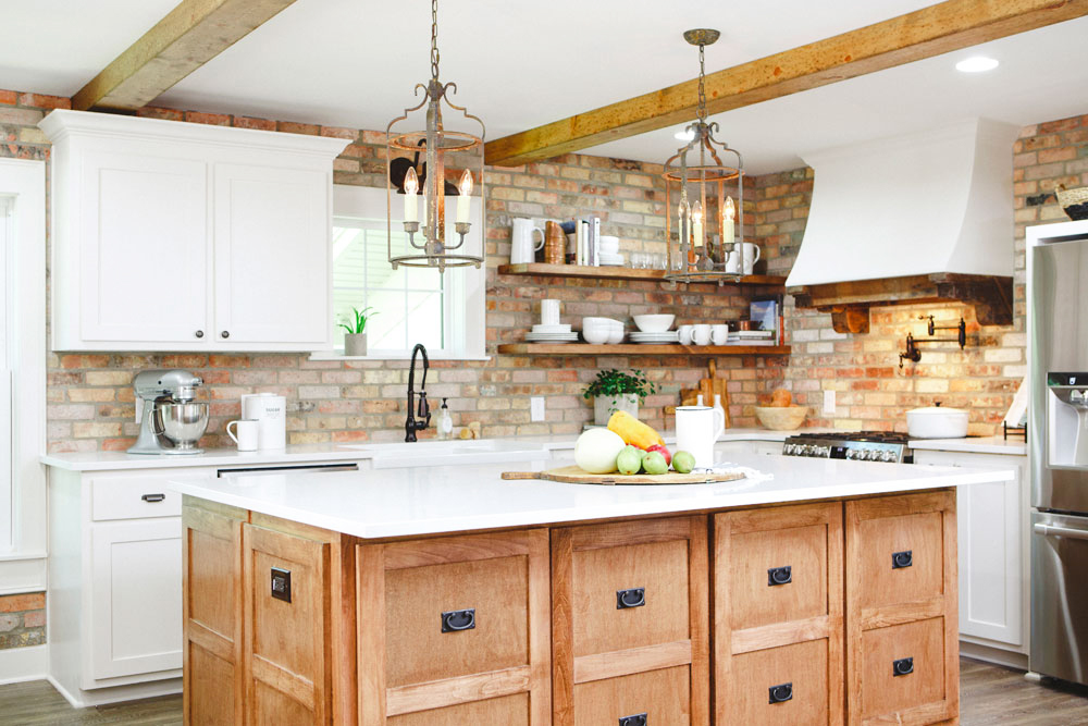 A rustic farmhouse-style open-concept kitchen with brick accent wall, wooden cabinetry and white marble countertops