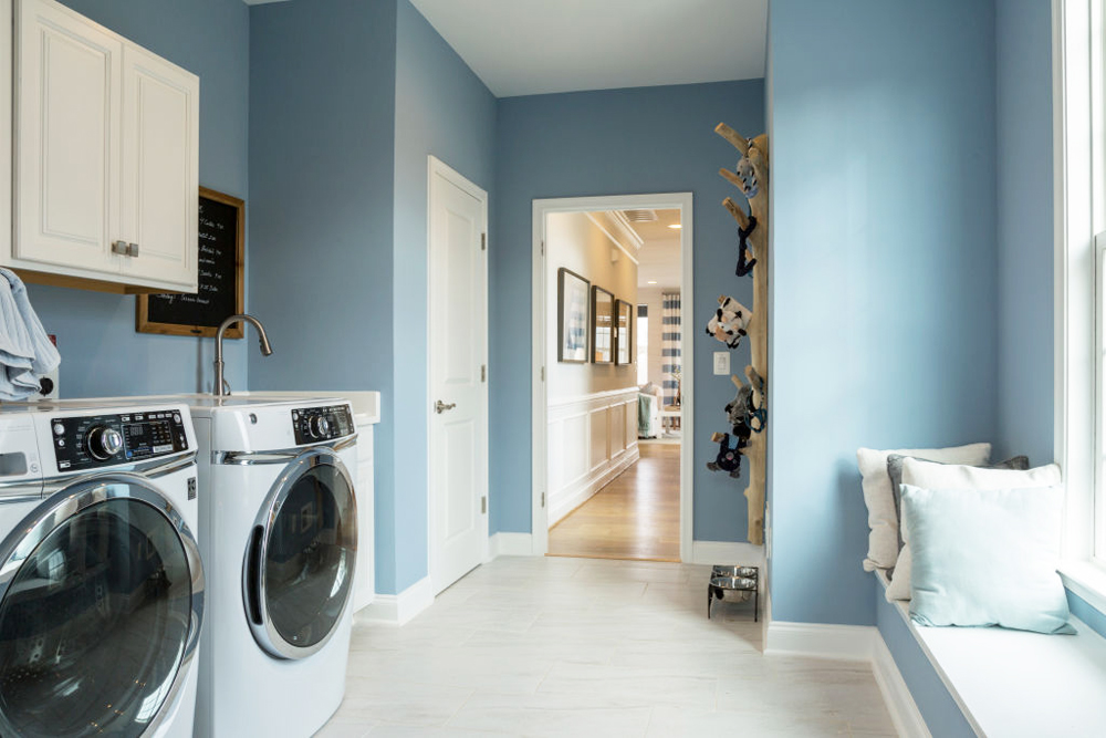 A pastel blue laundry room off the downstairs hallway with a window seat and washer/dryer