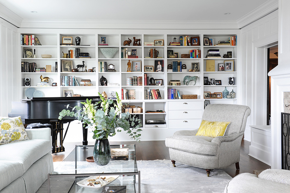 A white monochromatic living room with plush furniture, expansive bookshelf and a grand piano in the corner