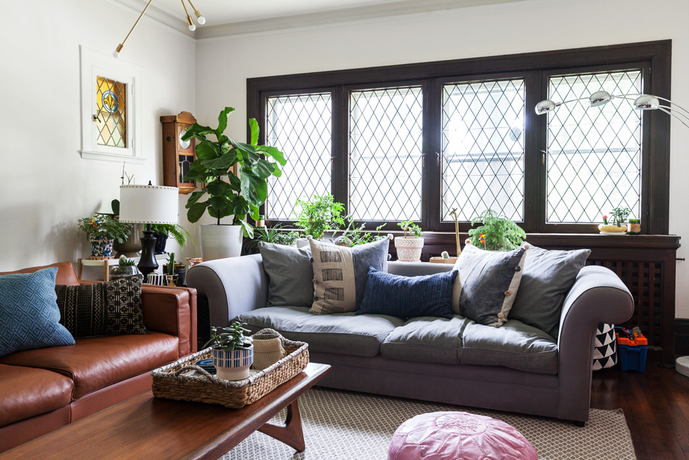 A brightly-lit living room with couches, coffee table and plenty of potted plants