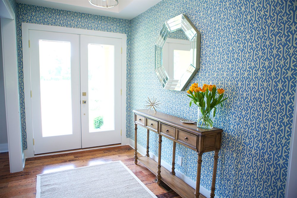 Entranceway with teal wallpaper and a contrasting wood console.