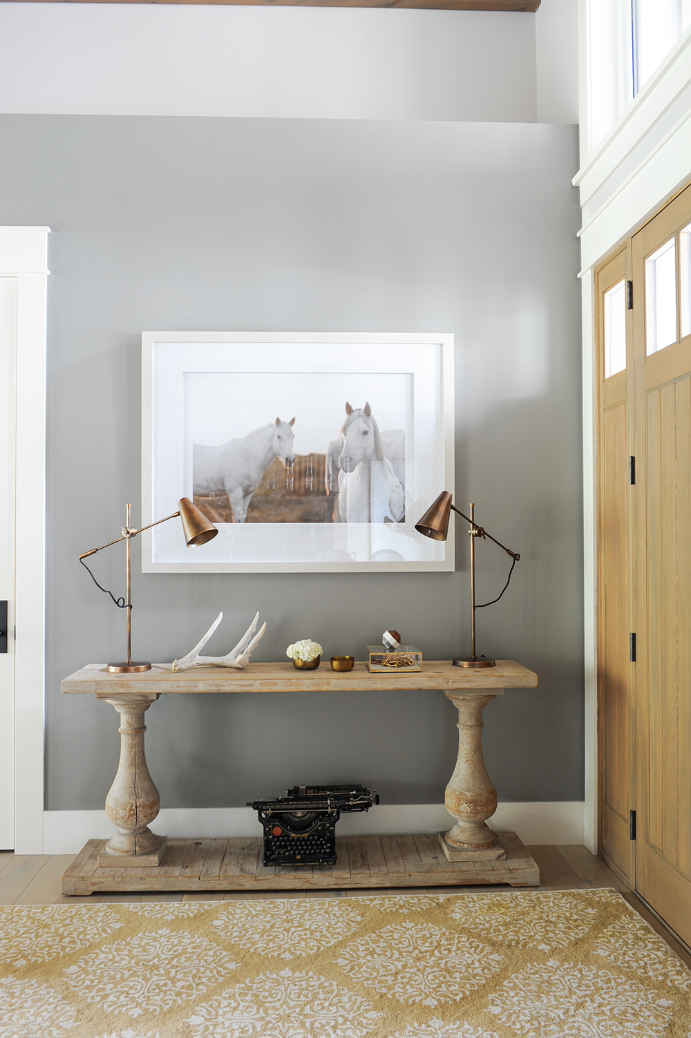 Stylish entryway with burnished brass lamps, rustic console, and equestrian artwork.