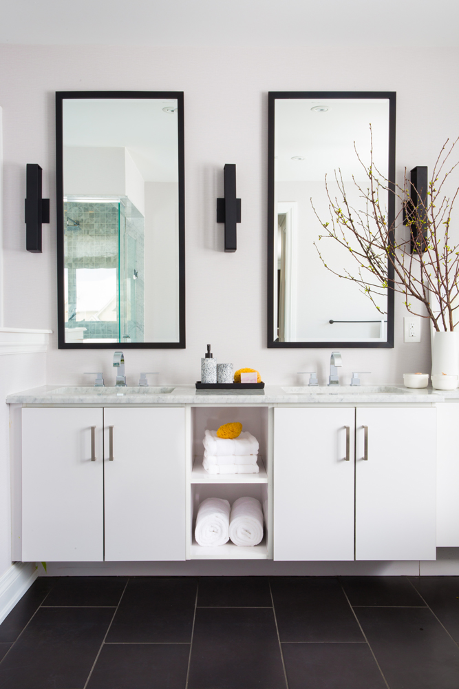 Bathroom with two mirrors and three black sconces over double floating vanity