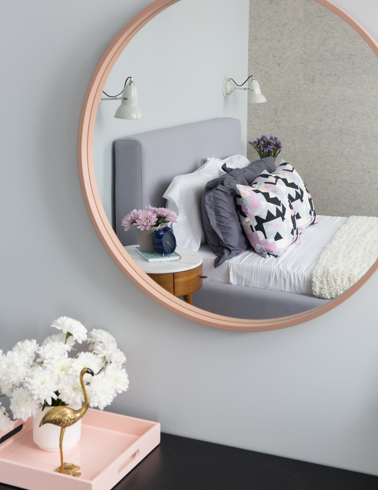 Bedroom reflected in round pink mirror, gold flamingo ornament