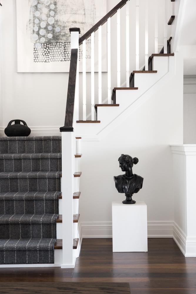 Staircase with grey striped runner, black bust on pedestal