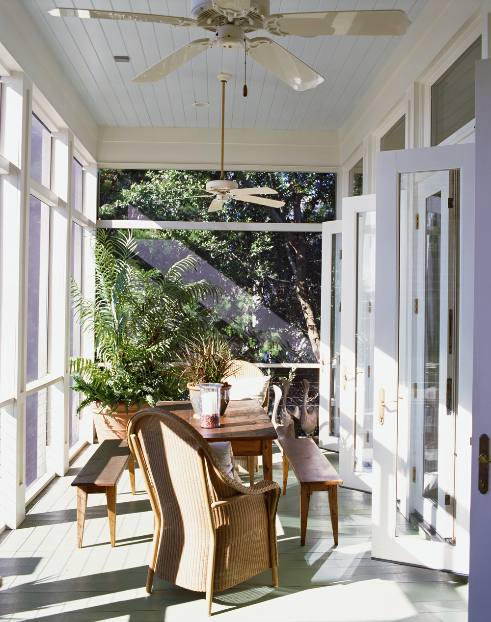 A narrow, bright sunroom with wooden picnic table for dining