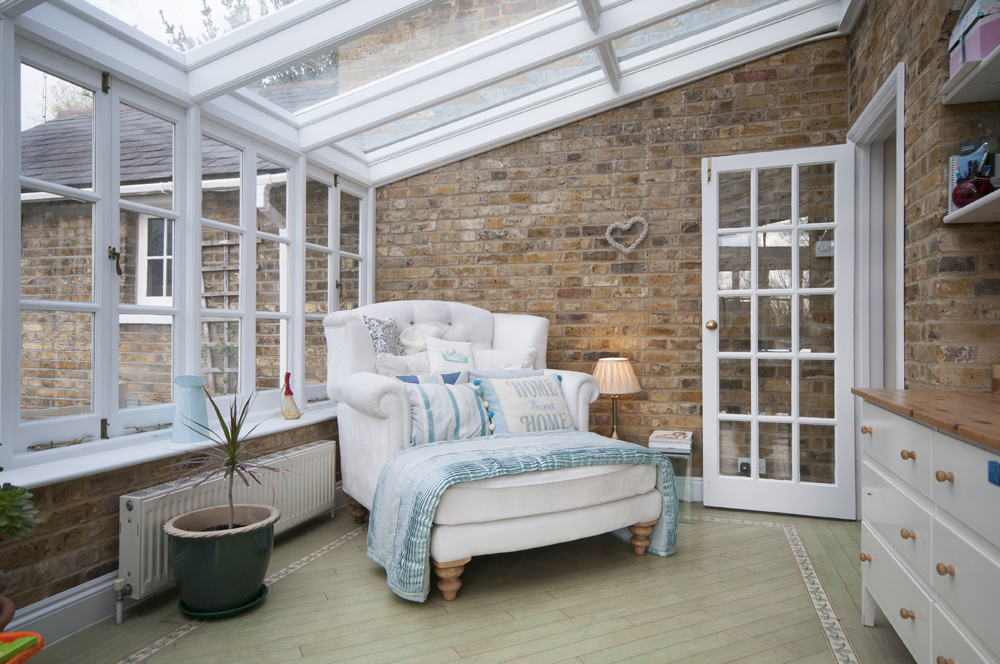 A brick sunroom with white chaise lounge chair and matching furniture and storage space