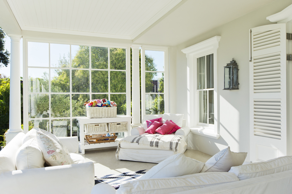 Mostly white sunroom with furniture, side tables and bright throw pillows
