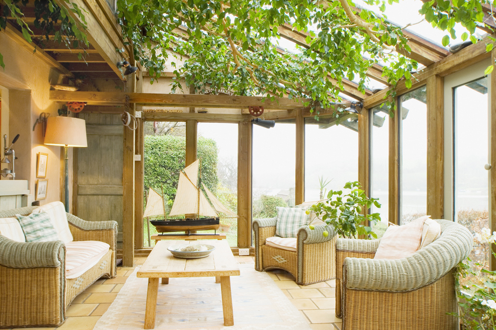 A rustic, wooden sunroom interior with wicker furniture and plenty of greenery