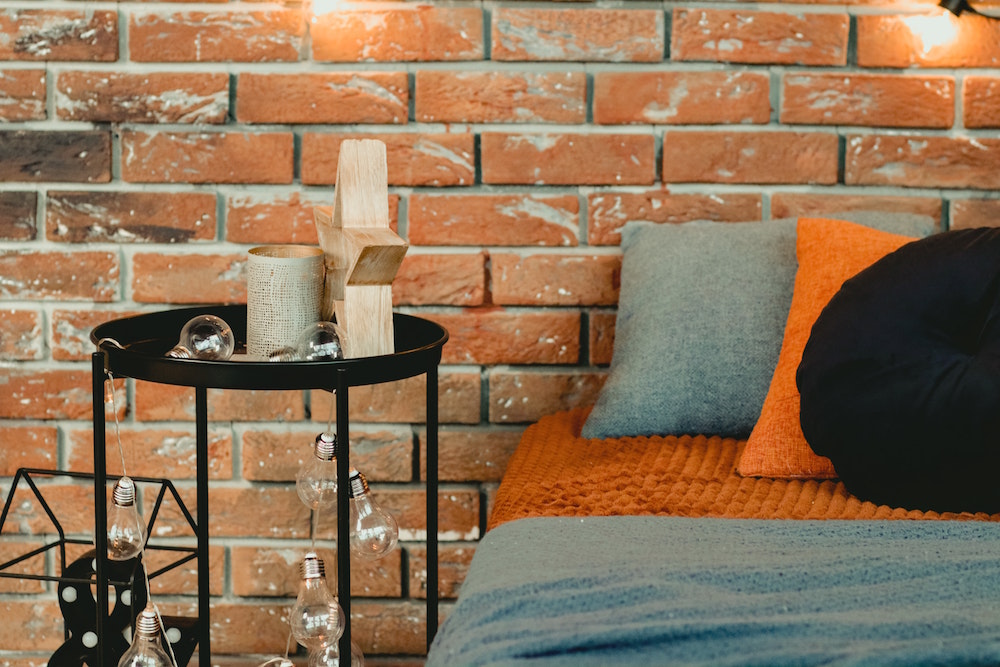 denim-blue bed with orange pillows in front of brick wall