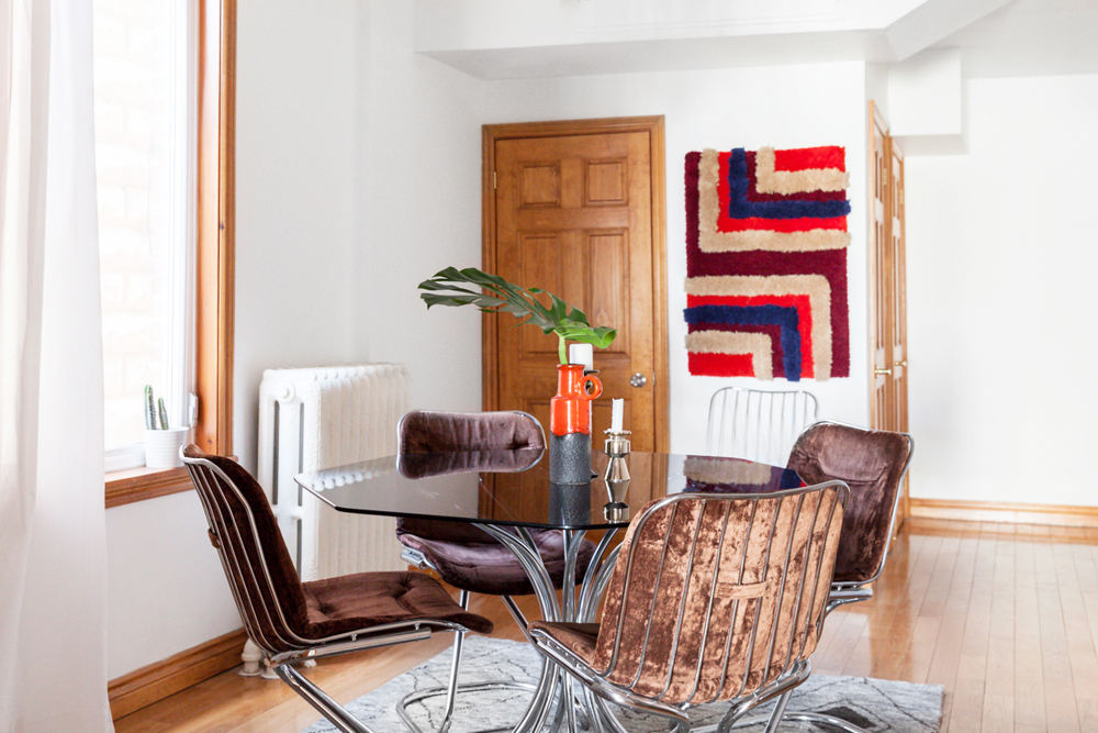 A dining room with a 1970s-era aesthetic, complete with velvet chair upholstery and macrame wall art
