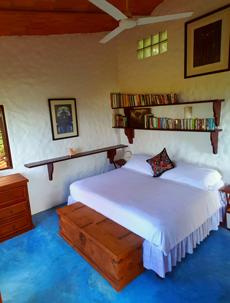 The bedroom in the treehouse with a sloped roof, blue carpet and double bed with bookshelf