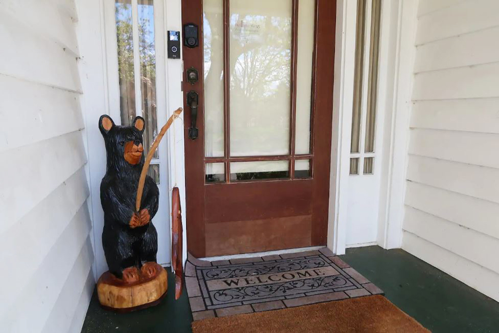Front porch with a wood bear statue and old Welcome mat
