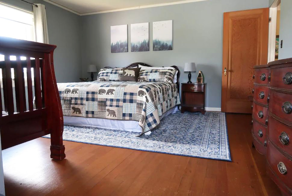 Spacious master bedroom with hardwood flooring, vintage cabinets, patterned rug and rustic quilt
