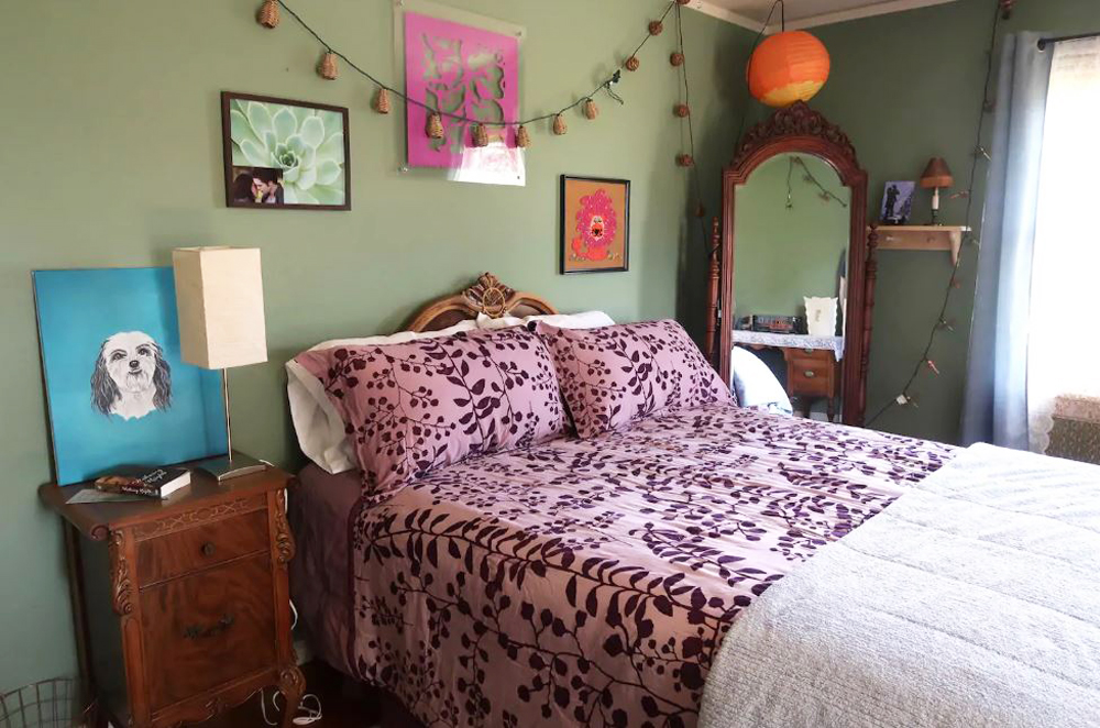 Eclectic bedroom with green wall paint, pink patterned bed quilt, mirrors and homemade artwork