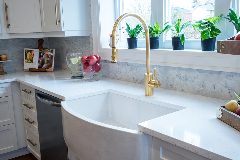 A farmhouse style sink with brass hardware in a brightly lit renovated kitchen