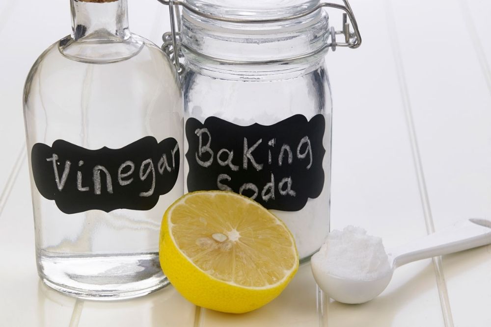 Clear glass bottle labelled Vinegar and Baking Soda in chalk, next to a scoop and lemon slice