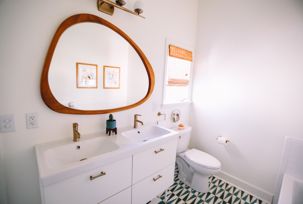 white bathroom with asymmetrical wood-frame vanity mirror