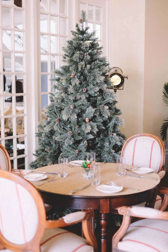 flocked green christmas tree with brown pinecones in front of set wooden dining table