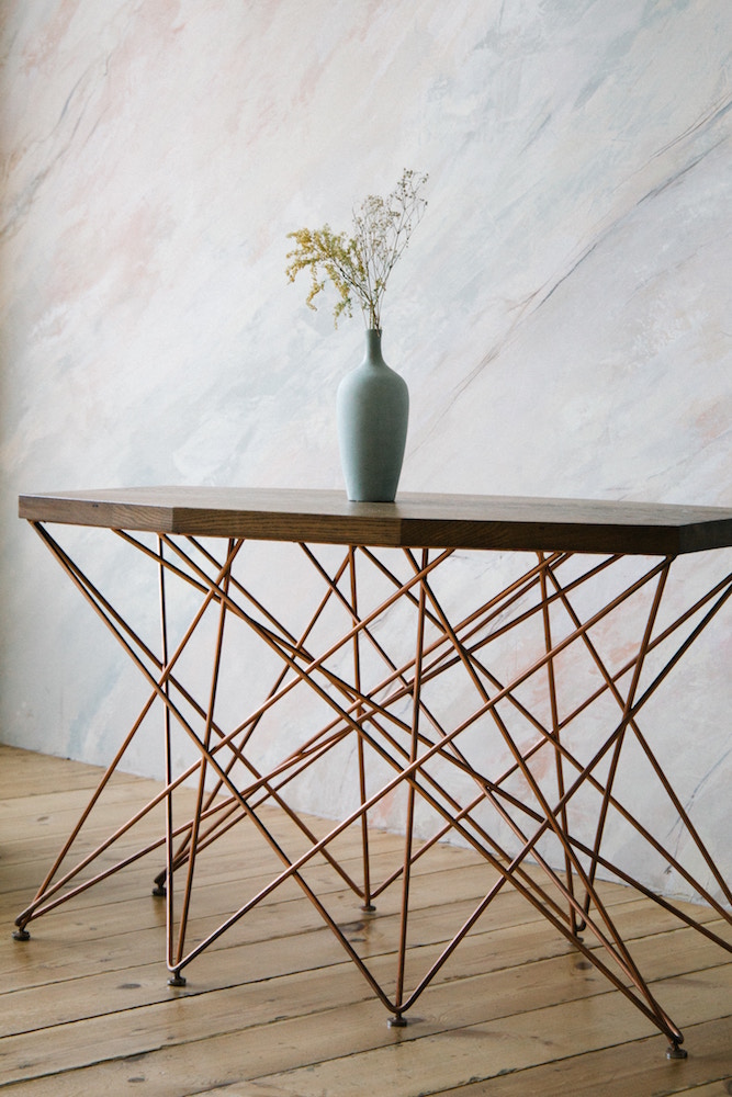 geometric table with vase in front of marble-finish wall