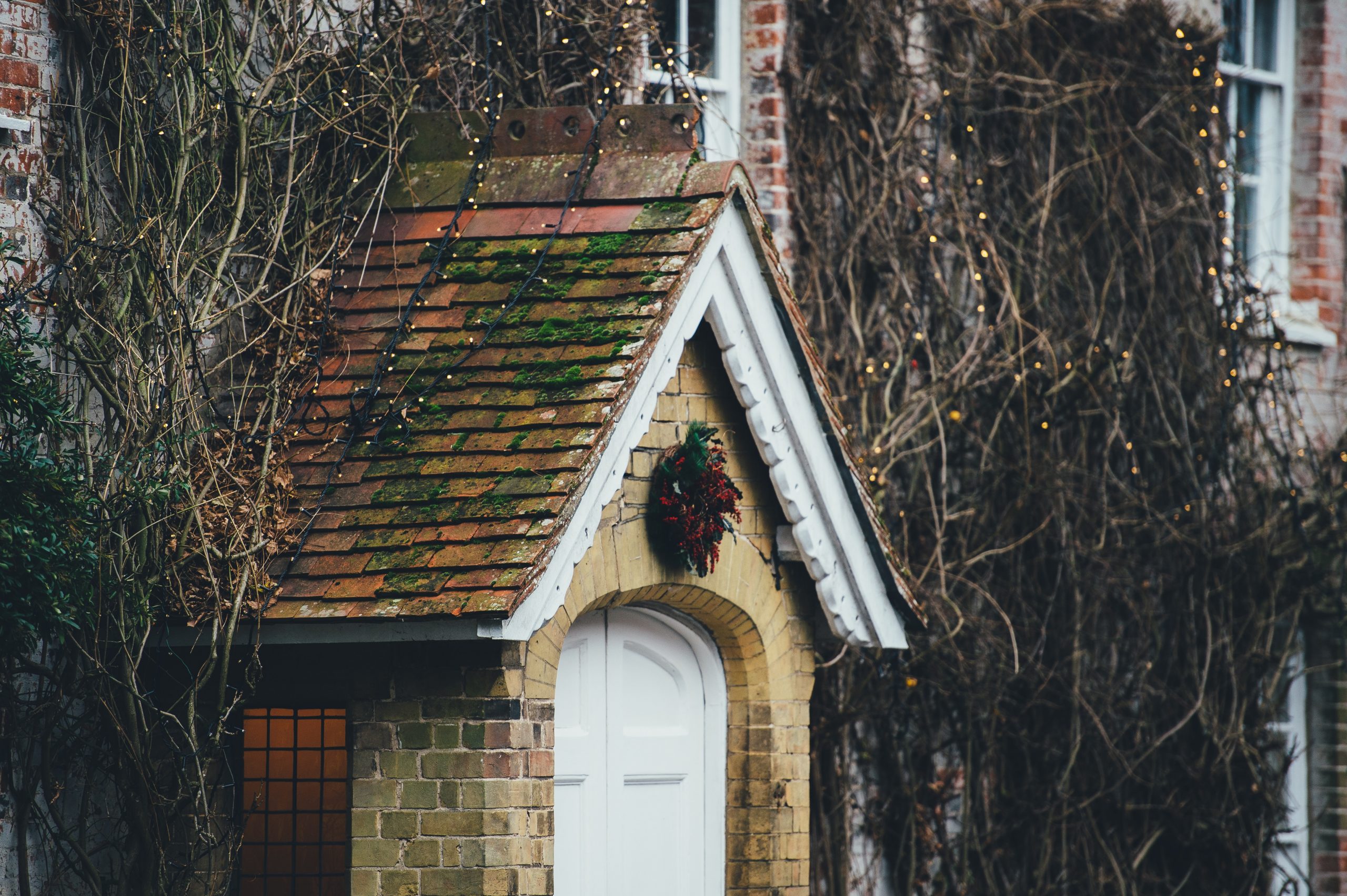 brick home exterior with white twinkle lights and branches on roof and wreath on door