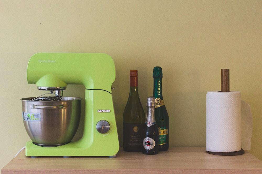 green stand mixer, bottles and paper towels on wooden counter