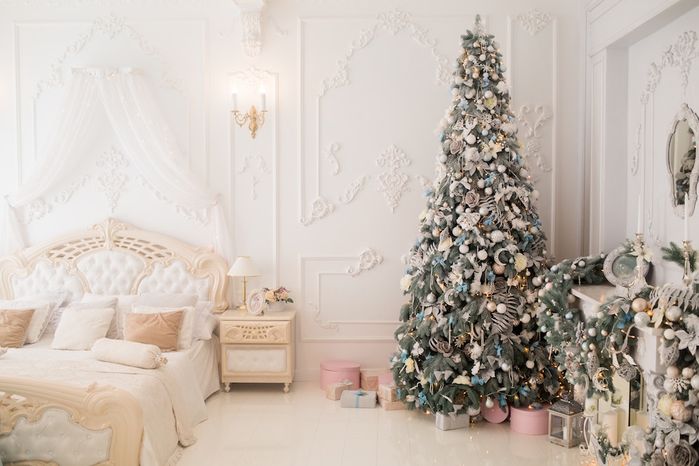 elegant white bedroom with white bed and green christmas tree with blue ornaments