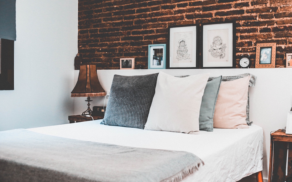White bedroom with exposed brick wall and pillows on bed